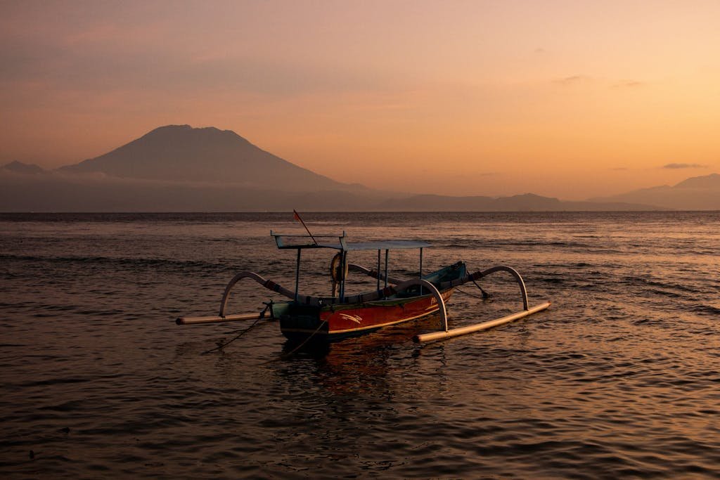 A serene view of a traditional boat against a mountain backdrop at sunset.
